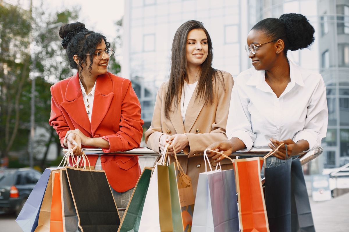 Trois personnes souriantes marchant dehors avec des sacs de shopping